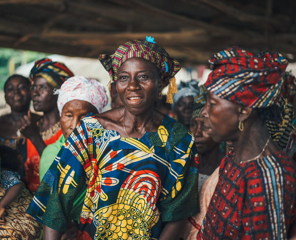 African woman in traditional clothing speaking to a community gathering